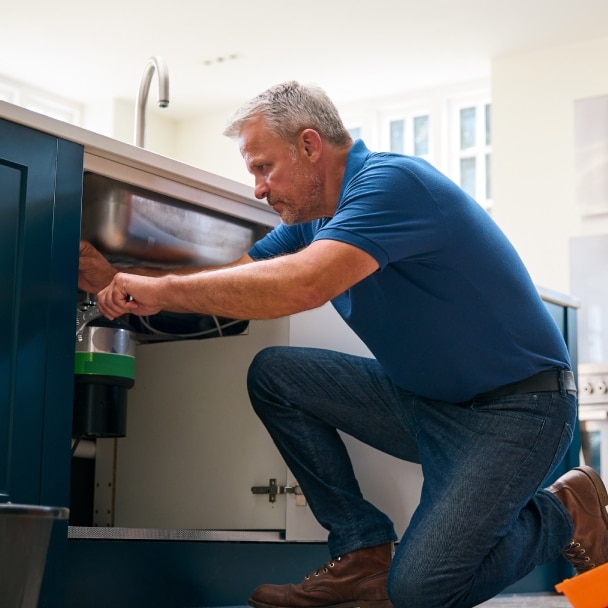 Middle-aged plumber fixing pipes under a kitchen sink.
